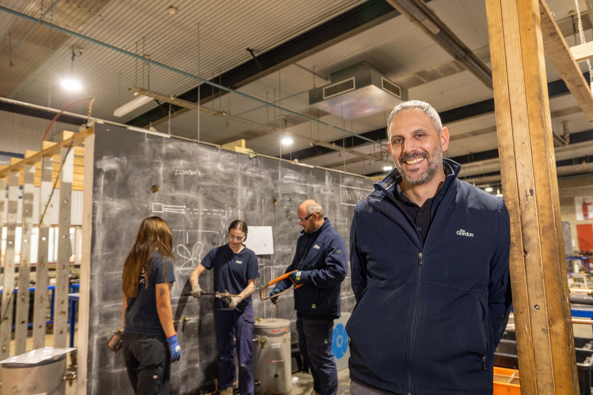 Article subject Andy standing in front of a small a group of other tradies in a work training environment.